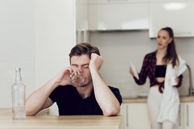 Betrunkener Mann in einer jungen Familie. Mann trinkt, während er an einem Tisch in der Küche sitzt