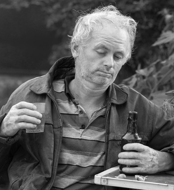 Betrunkener Mann mit Flasche Bier und Glas auf natürlichem Hintergrund