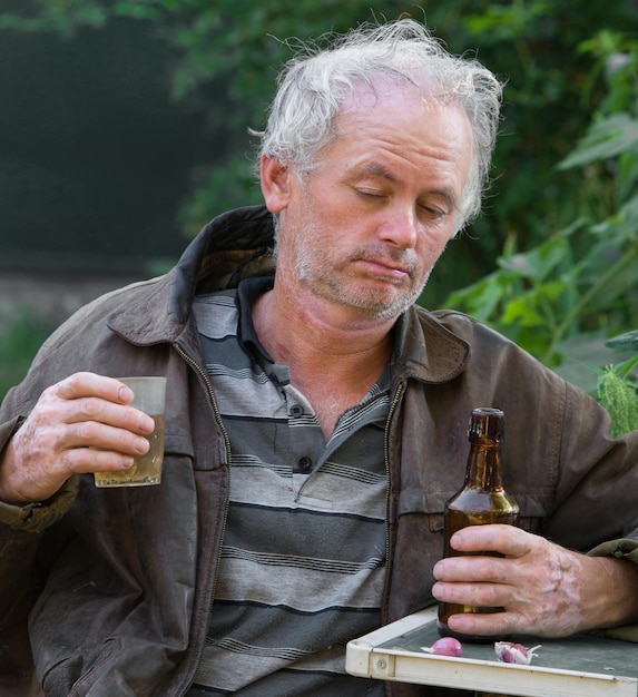 Betrunkener Mann mit Flasche Bier und Glas auf natürlichem Hintergrund