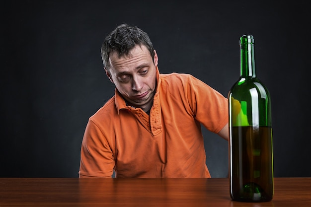 Betrunkener Mann schaut auf die Flasche Alkohol