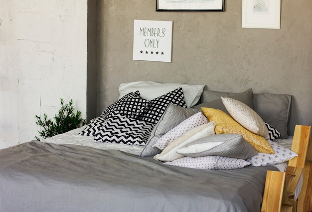 Bett mit Kissen auf dem Dachboden. Betonwände, Poster. Skandinavisches Interieur