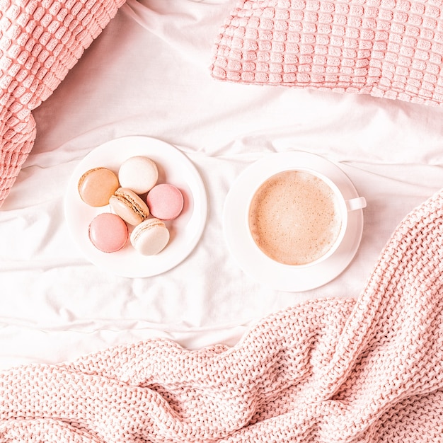 Bett mit rosa gestricktem plaid, kaffee und makronen