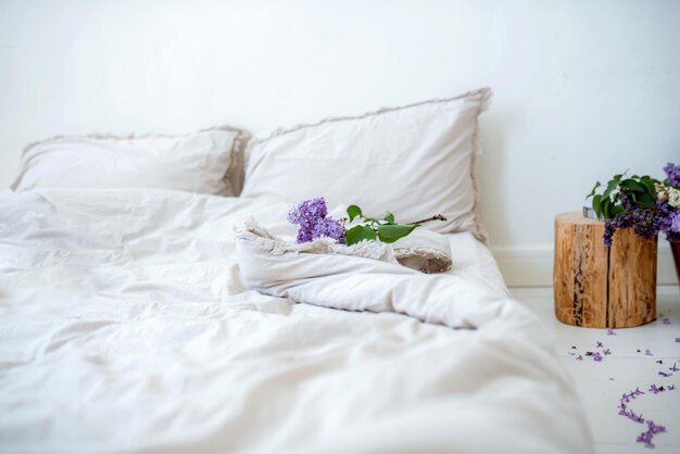 Foto bett mit schönen weißen, zerknitterten leinenbettwäsche in einem weißen schlafzimmer und lila blumen arbeiten im büro aus der ferne von zu hause aus auf dem bett fernunterricht online-bildung und arbeit