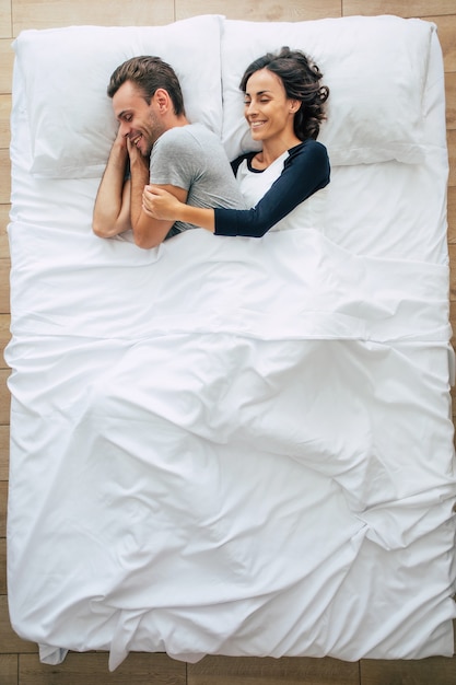Bettzeit. Die Familie schläft. Schönes junges verliebtes Paar liegt auf dem großen weißen Bett und ruht sich aus. Mann und Frau zusammen im Bett. Draufsichtfoto