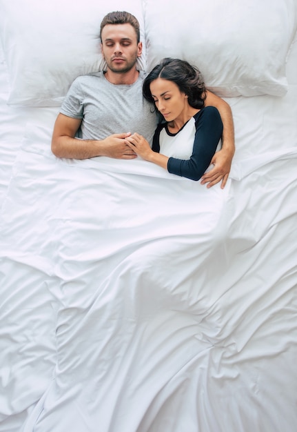 Bettzeit. Die Familie schläft. Schönes junges verliebtes Paar liegt auf dem großen weißen Bett und ruht sich aus. Mann und Frau zusammen im Bett. Draufsichtfoto