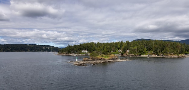 Bewaldete Insel mit Häusern, Booten und Docks in der Nähe einer kleineren Insel mit Leuchtturm