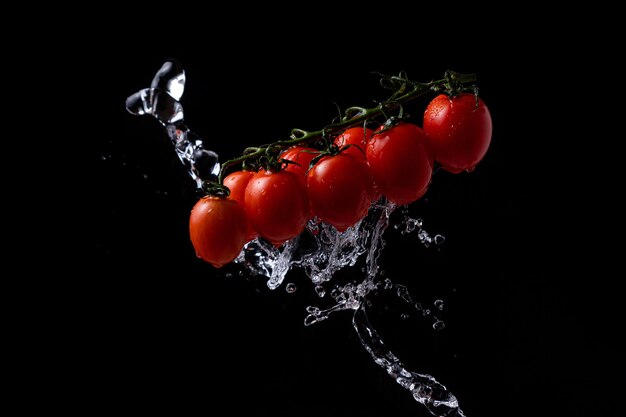 Bewegung einfrieren. Kirschtomaten auf schwarzem Hintergrund mit Spritzwasser