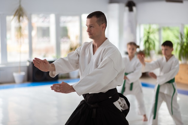 Bewegungen zeigen. Junger erfahrener Aikido-Trainer mit weißem Kimono, der die Bewegungen seiner Schüler zeigt