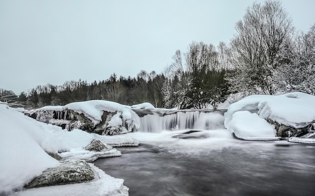 Bewölkter Morgen, Fluss im Winter, lange Belichtung macht Wasser milchig glatt, Schnee und Eis herum