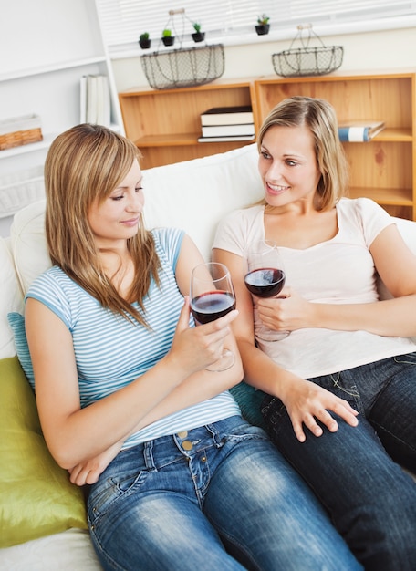 Bezaubern zwei Frauen, die den Wein sitzt auf einem Sofa trinken