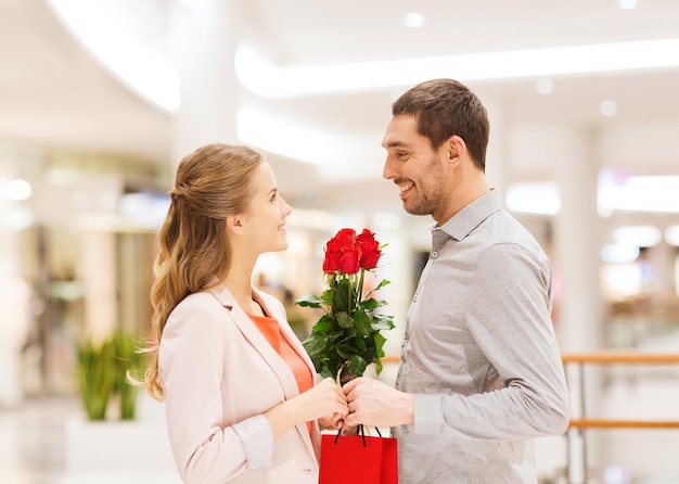 Beziehungen, Liebe, Romantik und People-Konzept - glückliches junges Paar mit Blumen, die im Einkaufszentrum sprechen