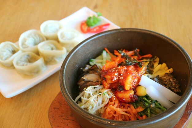 Bibimbap delicioso o cuenco de arroz mixto coreano con bolas de masa de mandu borrosas en segundo plano.