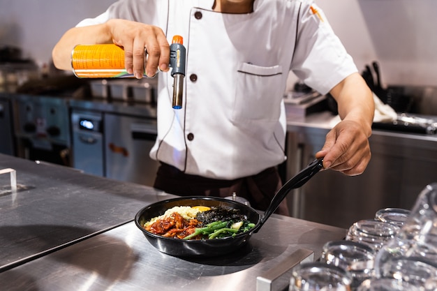 Bibimbap serviert auf der heißen Pfanne, die der Küchenchef mit einer Lötlampe zum Schmelzen von Mozzarella auf einem Spiegelei verwendet.