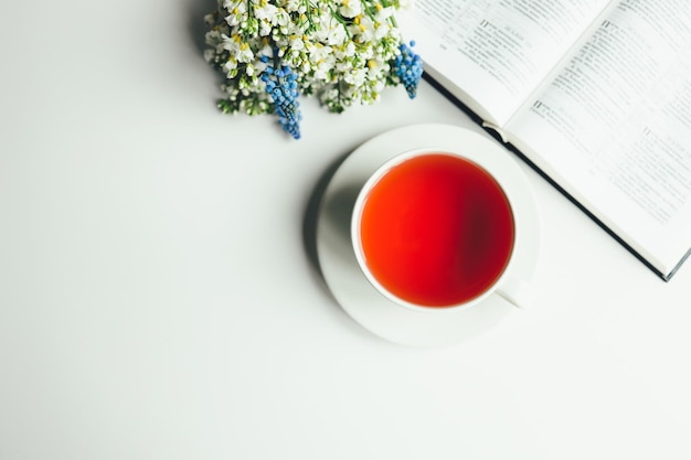 Bíblia aberta com flores e uma xícara de chá em um fundo branco