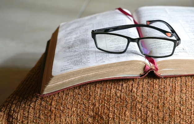 Bíblia aberta em um travesseiro com óculos de leitura em cima