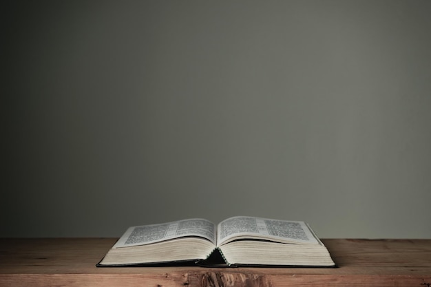 Biblia abierta en una mesa de madera roja y fondo de pared blanca Concepto religioso