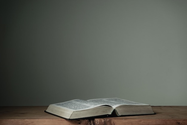 Biblia abierta en una mesa de madera roja y fondo de pared blanca Concepto religioso