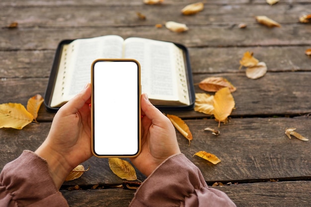 Biblia abierta y teléfono con pantalla aislada sobre fondo de madera