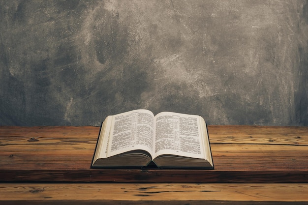 Biblia abierta en una vieja mesa de madera de roble Fondo de pared gris