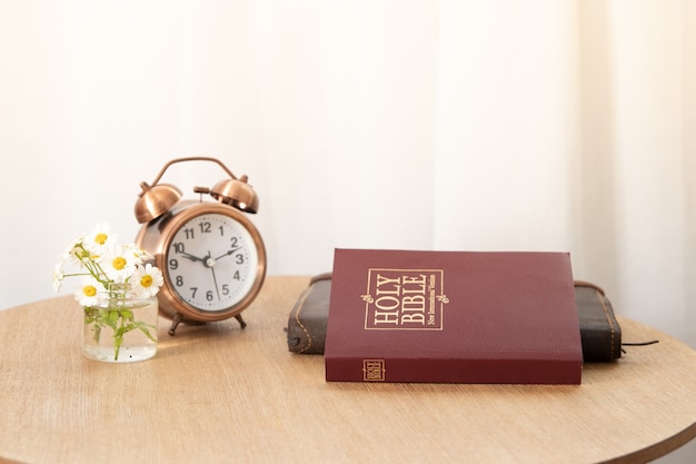 Bíblia e caderno na mesa com um despertador perto da janela. É hora de aprender o conceito da Bíblia