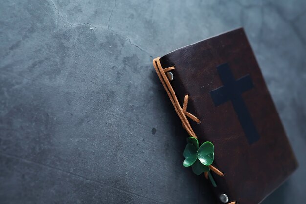 Una Biblia encuadernada en cuero sobre la mesa. Celebración religiosa cristiana irlandesa. Símbolo de trébol de cuatro hojas de buena suerte.