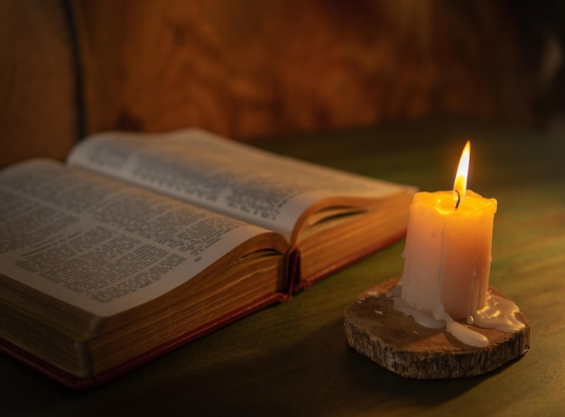 Foto bíblia iluminada com uma vela em um fundo de madeira conceito de religião e mensagem