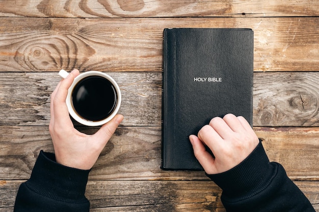 Biblia y una taza de café en manos masculinas sobre un fondo de madera vista superior concepto de cristianismo y religión