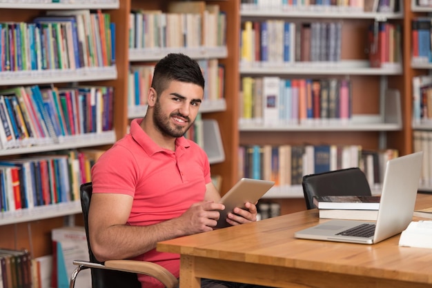 En la biblioteca Estudiante árabe guapo con computadora portátil y libros que trabajan en una biblioteca universitaria de secundaria Profundidad de campo