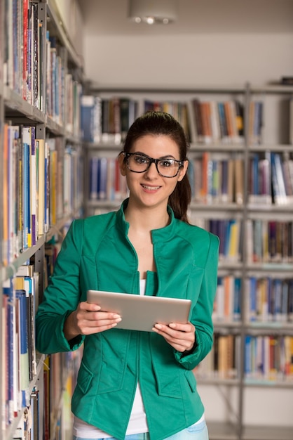 En la biblioteca Estudiante bastante femenina con tableta y libros que trabajan en una biblioteca universitaria de secundaria Profundidad de campo reducida