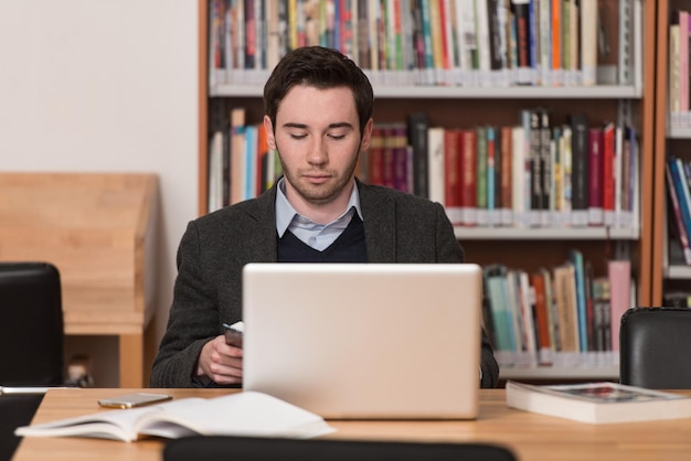 En la biblioteca Estudiante masculino guapo con computadora portátil y libros que trabajan en una biblioteca universitaria de secundaria Profundidad de campo