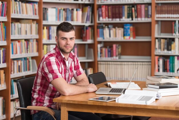 En la biblioteca Estudiante masculino guapo con computadora portátil y libros que trabajan en una biblioteca universitaria de secundaria Profundidad de campo