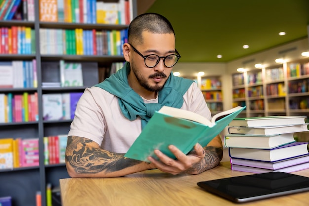 En biblioteca. Hombre asiático leyendo un libro en la biblioteca