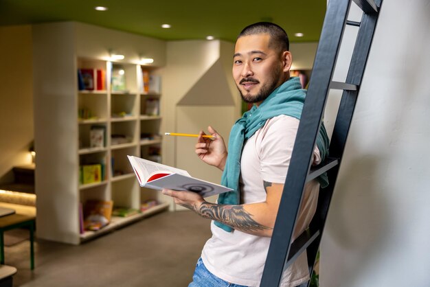 Foto en biblioteca. joven estudiante asiático parado al lado de la escalera