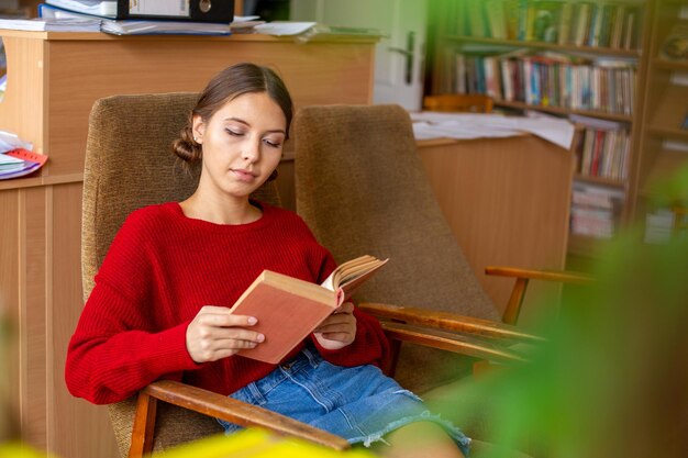 Biblioteca de la universidad hermosa chica caucásica sentada en la silla junto a la estantería