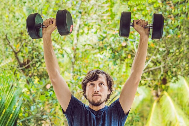 Foto bicep curl - homem de fitness de treinamento de peso fora de trabalhar os braços levantando halteres, fazendo bíceps curls. modelo esportivo masculino, exercício ao ar livre como parte do estilo de vida saudável.