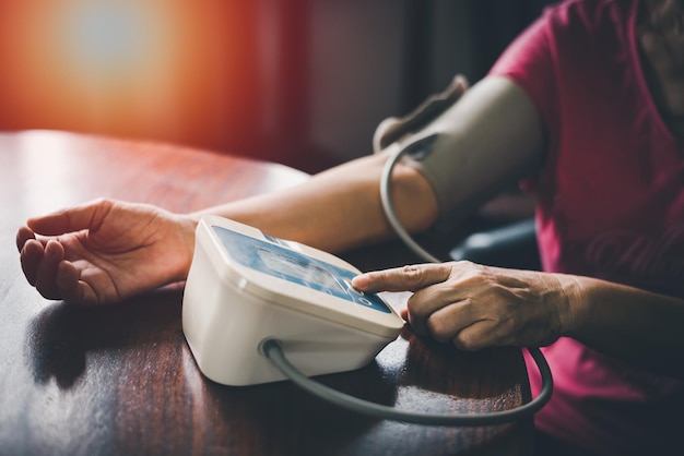 Foto bíceps de braço de mulher mais velha no manguito senhora aposentada mais velha medindo manualmente a pressão arterial usando máquina de tonômetro digital em casa conceito de tratamento de doenças de saúde