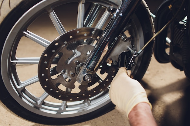 Bicicleta de fixação do homem. homem novo seguro que repara a motocicleta perto de sua garagem.