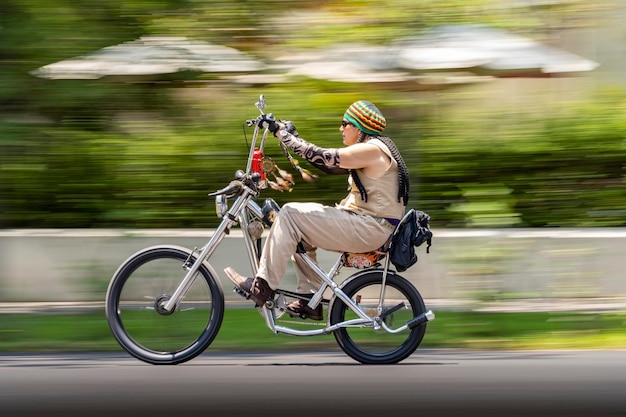 Bicicleta de homem com dreadlocks e manga de tampa rastafari simulando tatuagens custom chopper bike movimento borrado