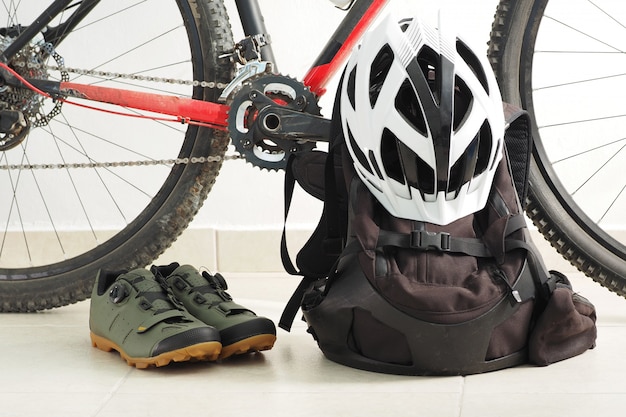 Foto bicicleta de montanha, sapatos velo, mochila e capacete branco em casa.