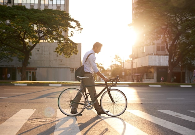 Bicicleta e homem de negócios na cidade para viagens matinais e pegada de carbono Transporte de bicicleta e urbano com funcionário do sexo masculino andando na faixa de pedestres para trânsito de viagem e profissional