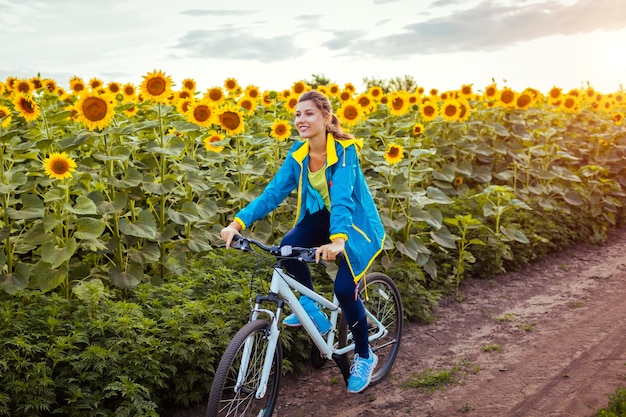 Bicicleta feliz nova da equitação do ciclista da mulher no campo do girassol.