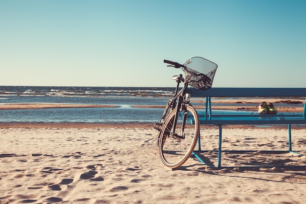 Bicicleta fica perto do banco na praia contra o marretro foto em tons