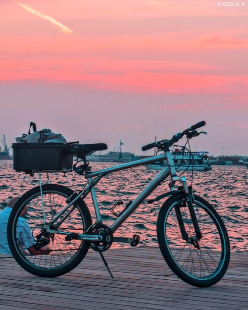 Foto bicicleta pelo mar contra o céu durante o pôr do sol