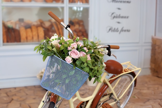 bicicleta velha com uma cesta de rosas contra a parede em tons pastel. Suporte de bicicleta decorativo para plantas e flores.