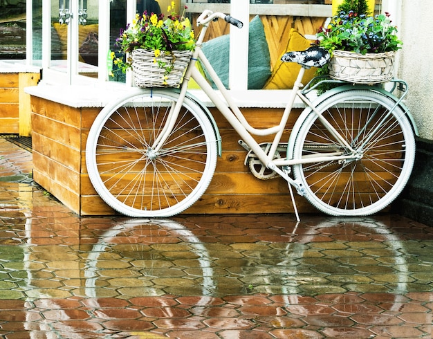 Bicicleta vintage branca com cestas florais do lado de fora no fundo do café. Transporte de estilo retro com lindas flores