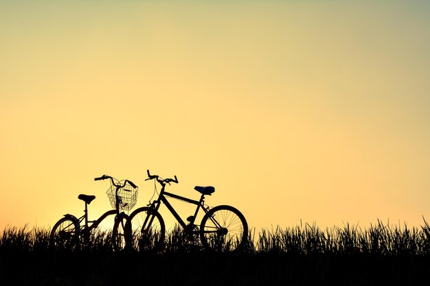 Foto bicicletas de silueta en medio de la hierba contra un cielo naranja claro durante la puesta de sol