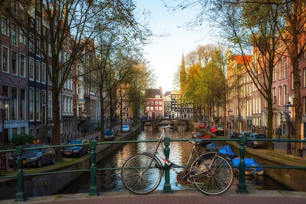 Bicycle na ponte com as casas e o canal holandeses tradicionais de amsterdão em amsterdão, países baixos.