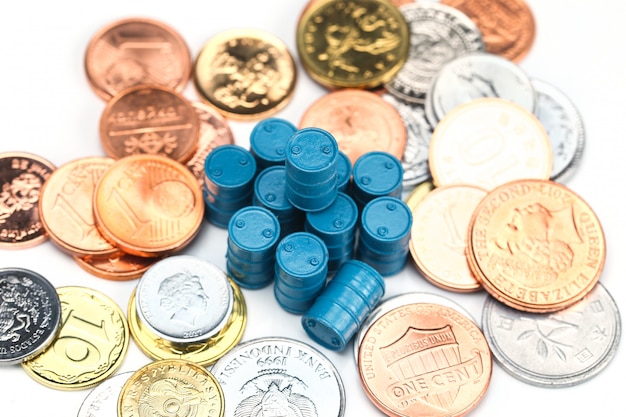 Foto bidones de aceite azul y monedas sobre fondo blanco.