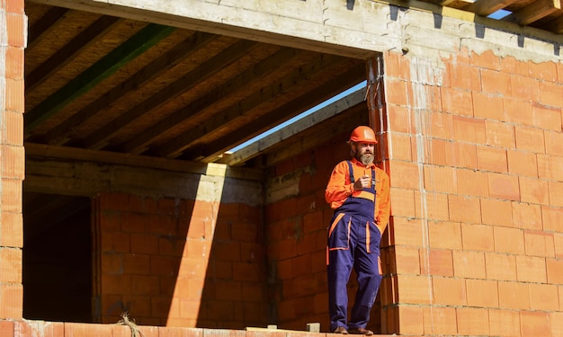 Bien hecho Reparador cansado constructor relajándose en el sitio de construcción Constructor fumando cigarrillo Descanso y relájese Hombre barbudo en uniforme de ingeniero y casco Día normal Rutina diaria en la construcción