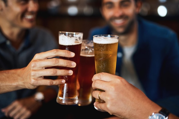 Foto bien merecido y listo para beber primer plano de un grupo de jóvenes amigos sentados juntos en una mesa mientras disfrutan de una cerveza y celebran con un brindis de celebración dentro de un bar